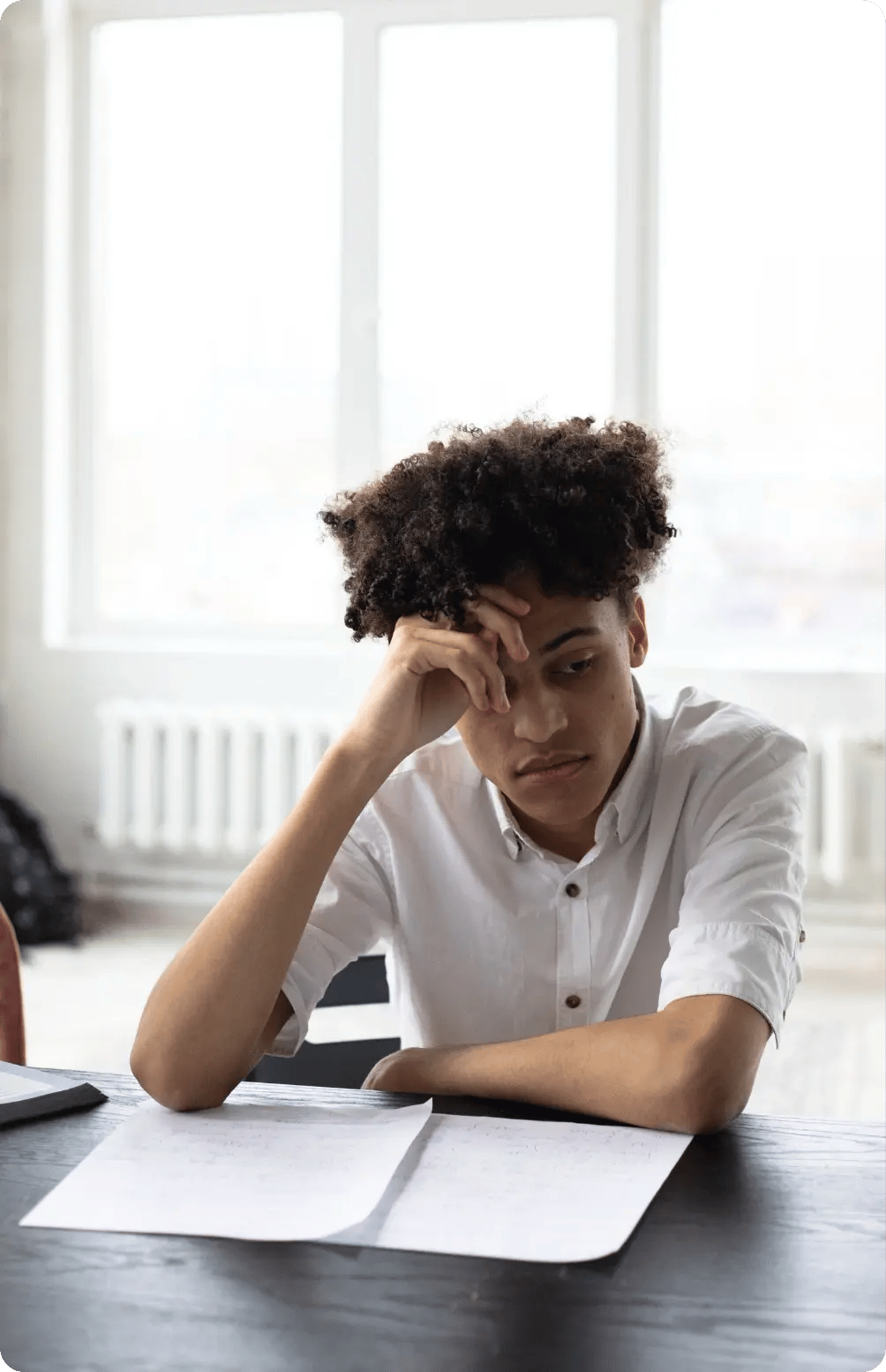 A young male student sitting at a desk resting his head on his hand in frustration, looking down at handwritten pages while struggling to write a unique college essay. A young male student sitting at a desk resting his head on his hand in frustration, looking down at handwritten pages while struggling to write a unique college essay.