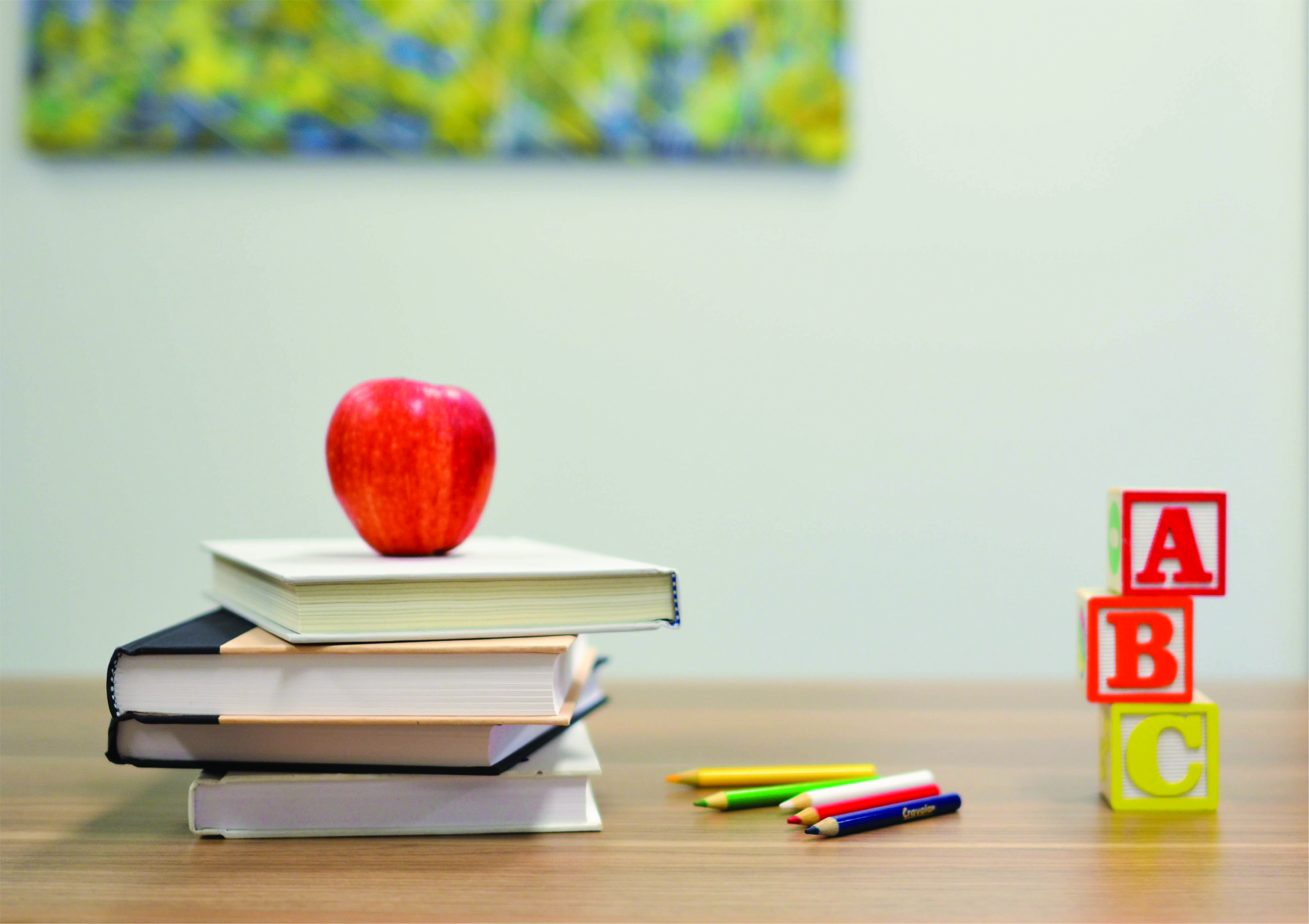High school desk with a stack of books, an apple, and ABC blocks.
